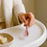 Person holding a pink fork over a plate with food on a white tray.